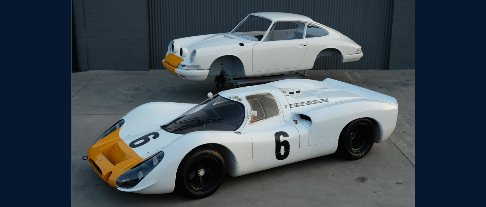 The Emory Outlaw 911K is lifted behind the car serving as its design inspiration, the Porsche 908.