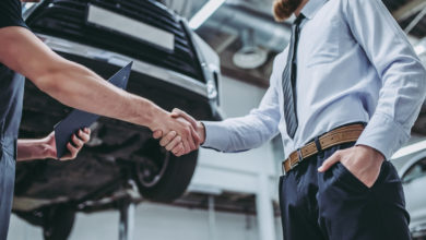 Handsome businessman and auto service mechanic are discussing the work and shaking hands. Car repair and maintenance.