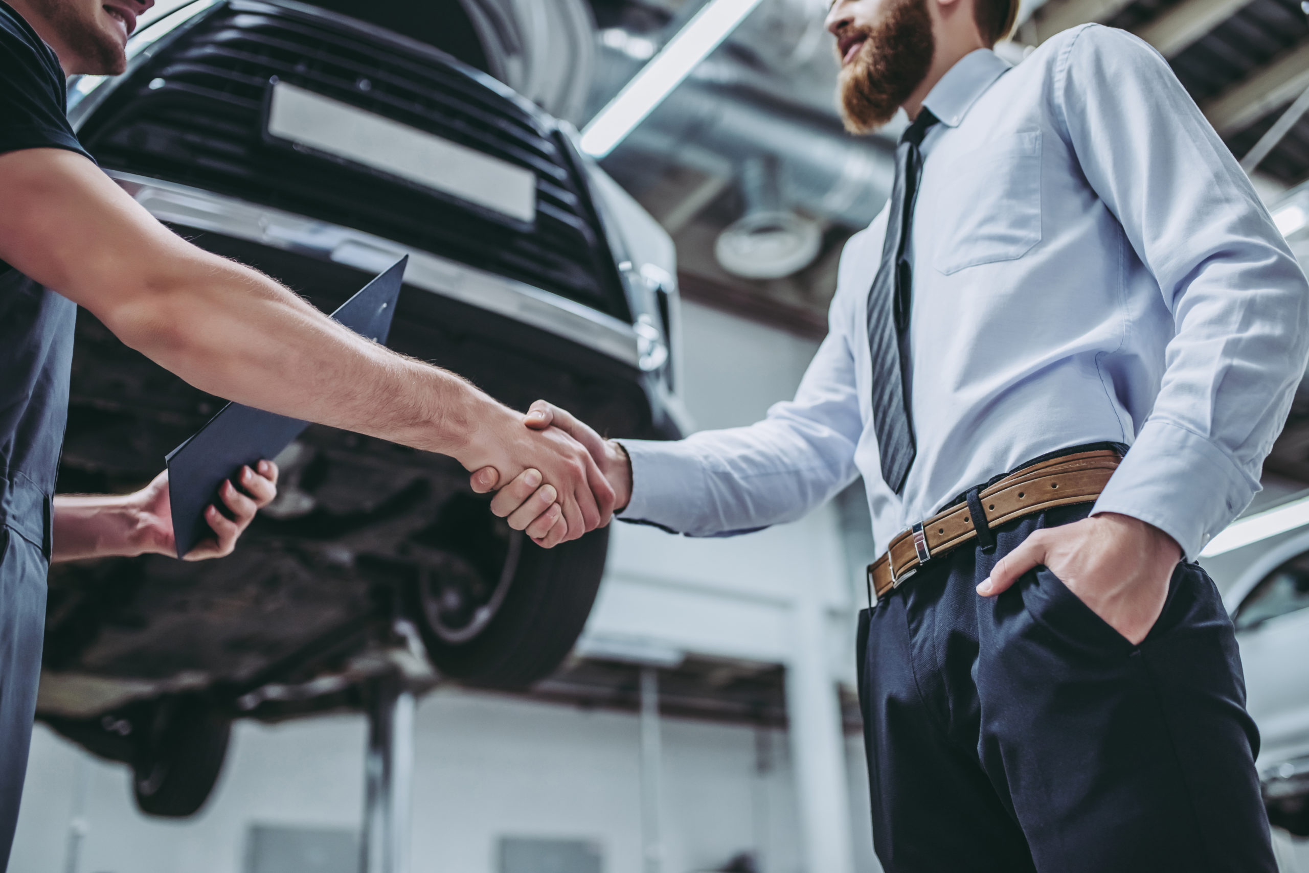 Handsome businessman and auto service mechanic are discussing the work and shaking hands. Car repair and maintenance.