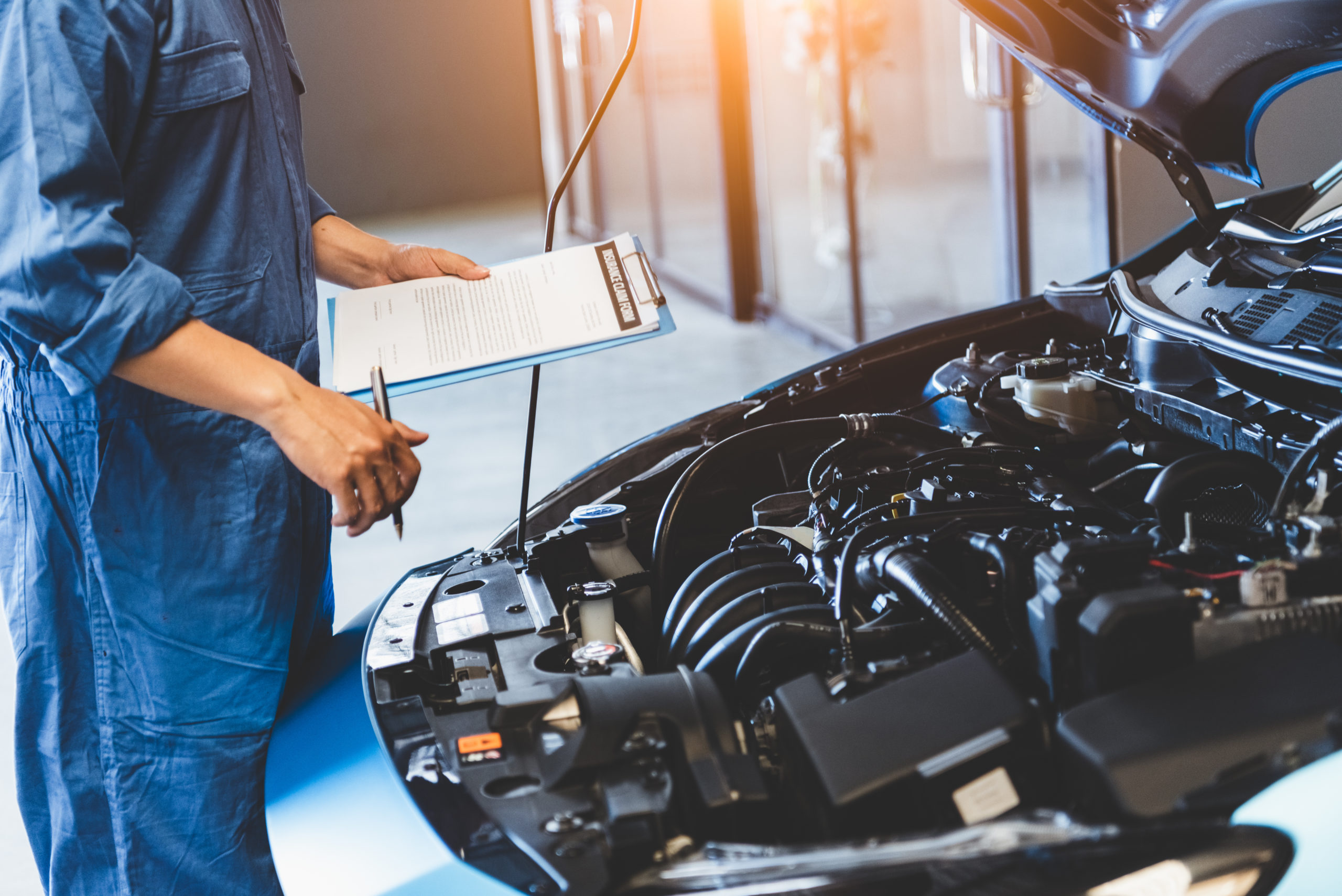 Car mechanic holding clipboard and checking to maintenance vehicle by customer claim order in auto repair shop garage. Engine repair service. People occupation and business job. Automobile technician