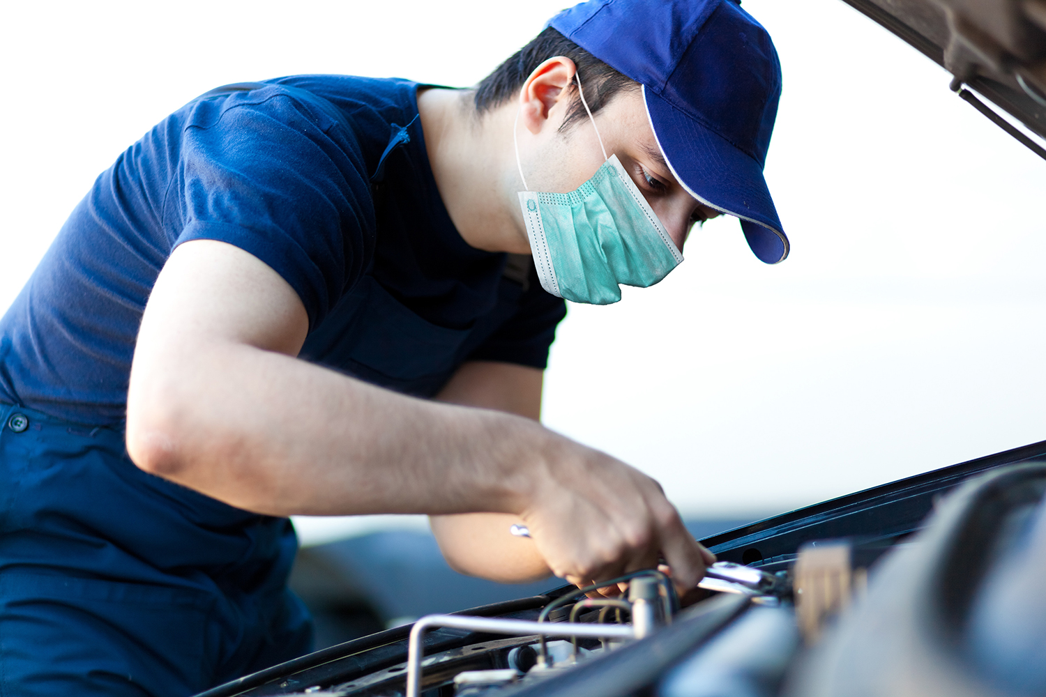 Mechanic fixing a car engine wearing a mask, coronavirus concept