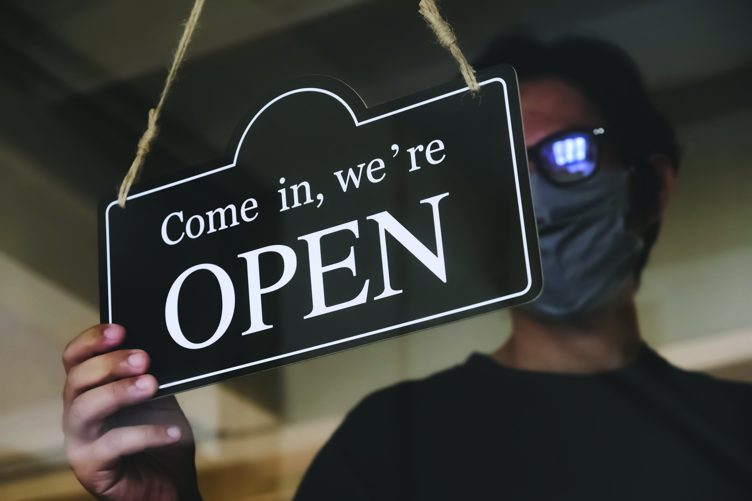 the state allows retail stores or restaurants and businesses to reopen after coronavirus restrictions. man with face mask turning a sign on a door shop. economy starts running after being on lockdown.