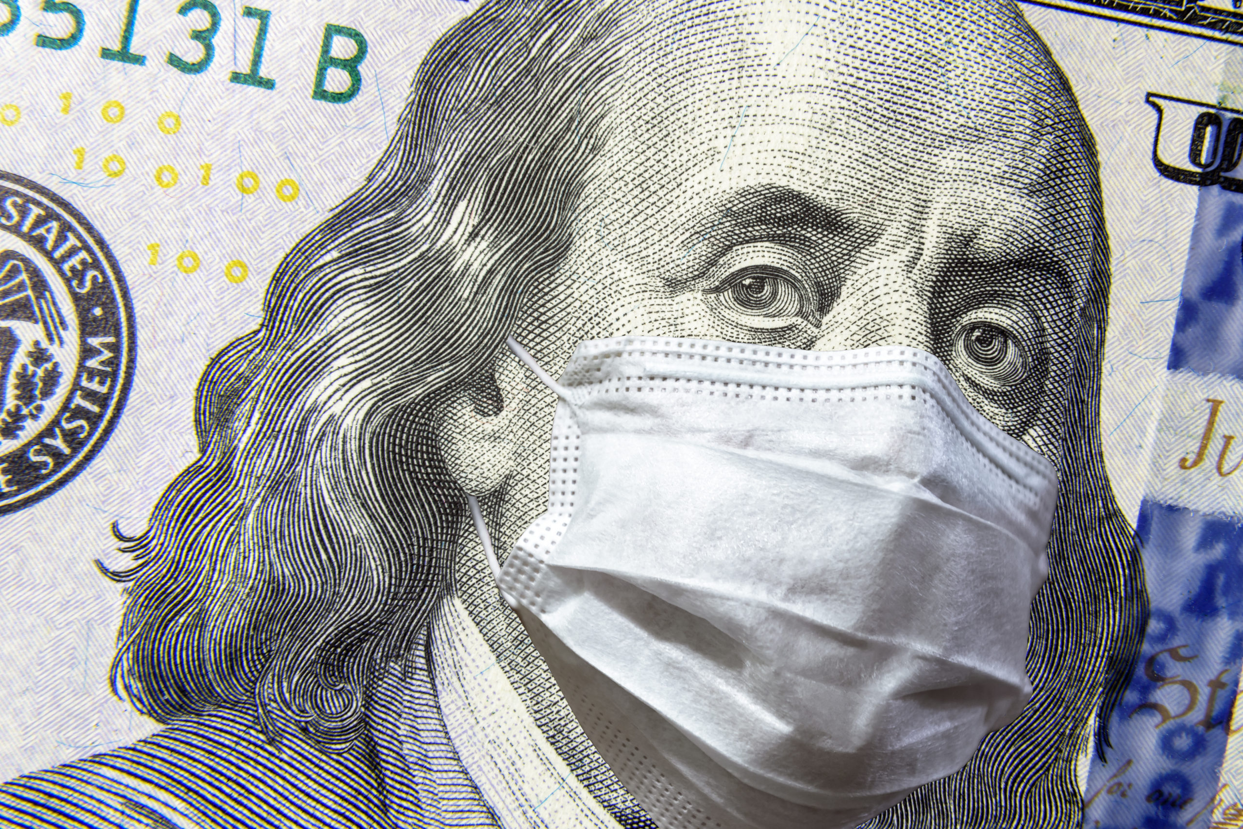 COVID-19 coronavirus in USA, 100 dollar money bill with face mask. COVID-19 affects global stock market. World economy hit by corona virus outbreak and pandemic fears. Crisis and finance concept.