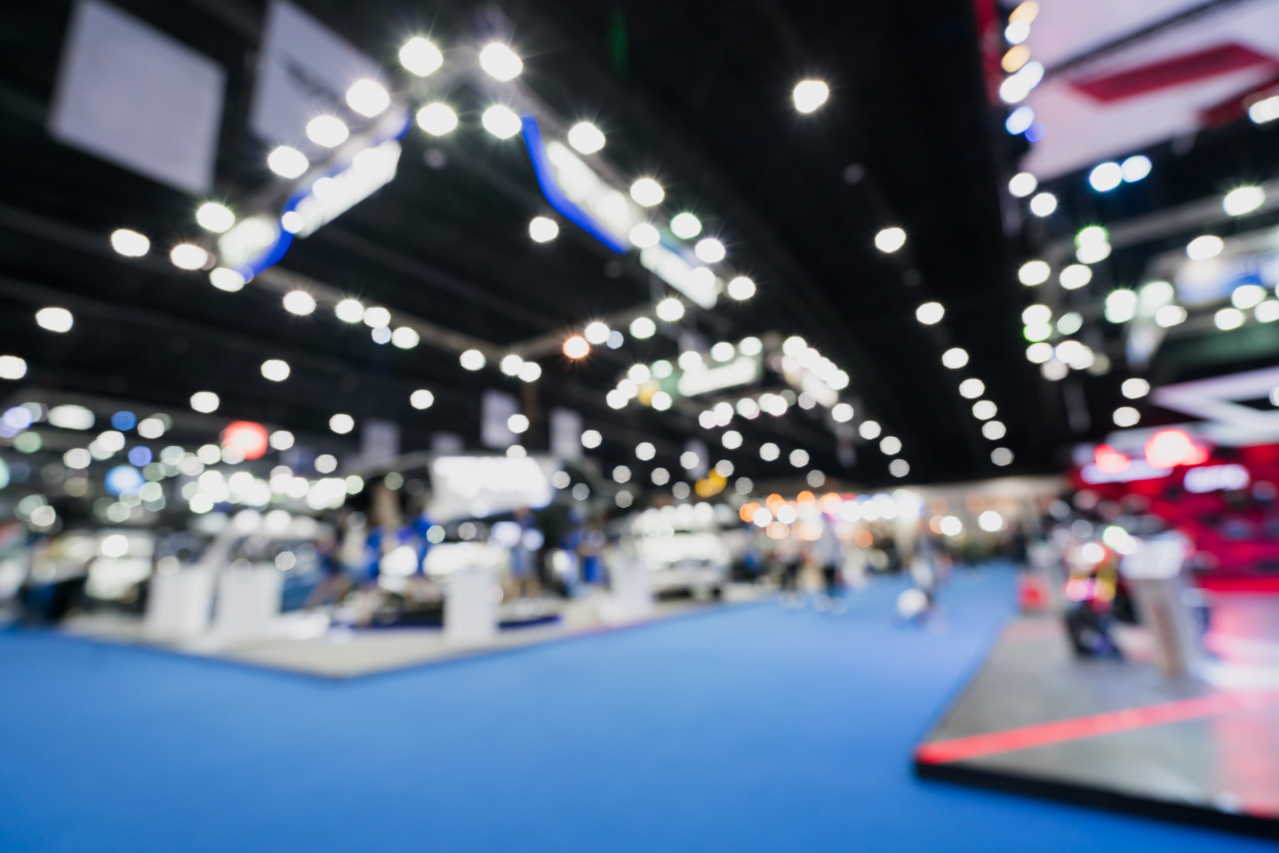 Blurred, defocused background of public event exhibition hall showing cars and automobiles, business commercial event concept