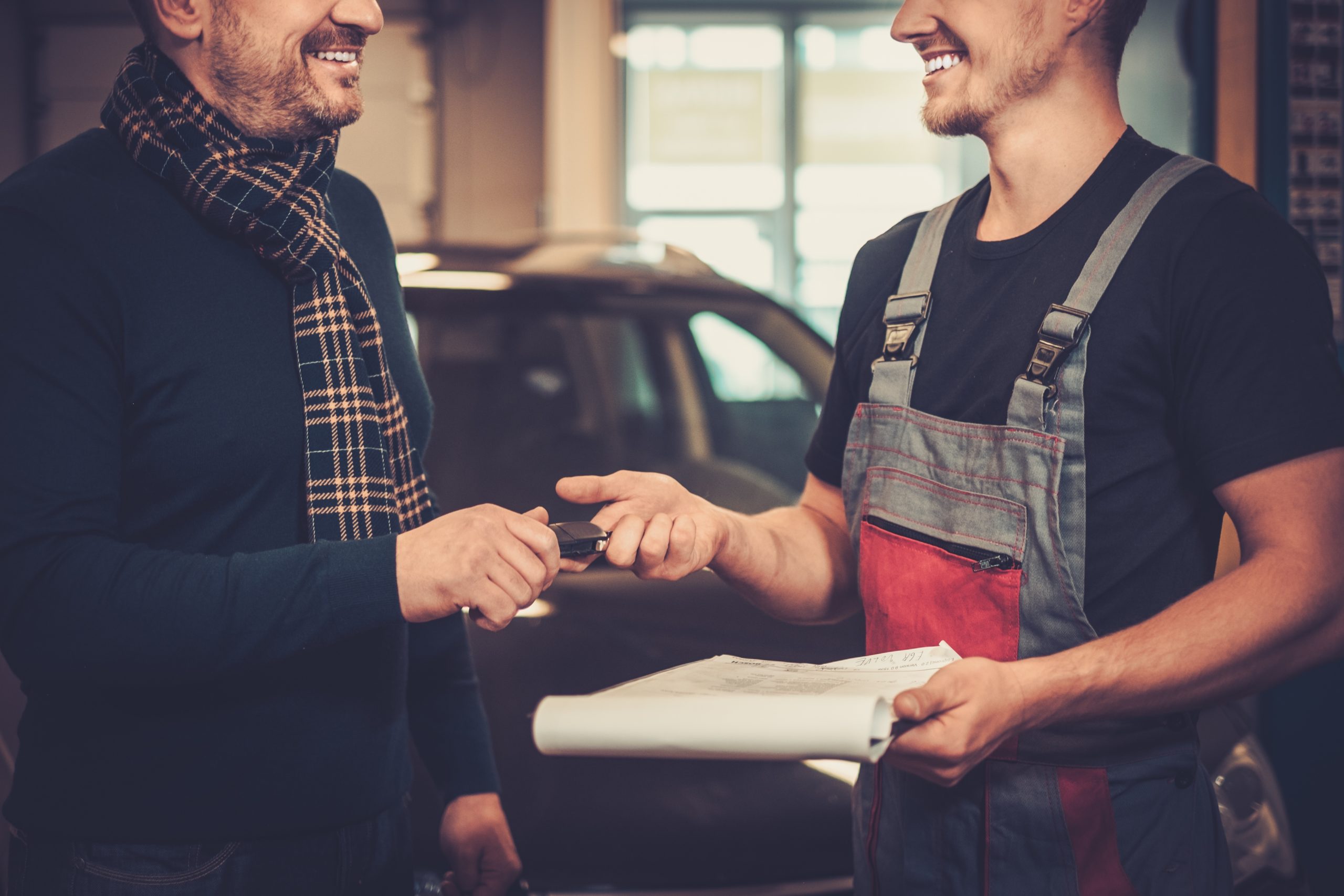 Professional car mechanic giving client keys to his repaired car in auto repair service.