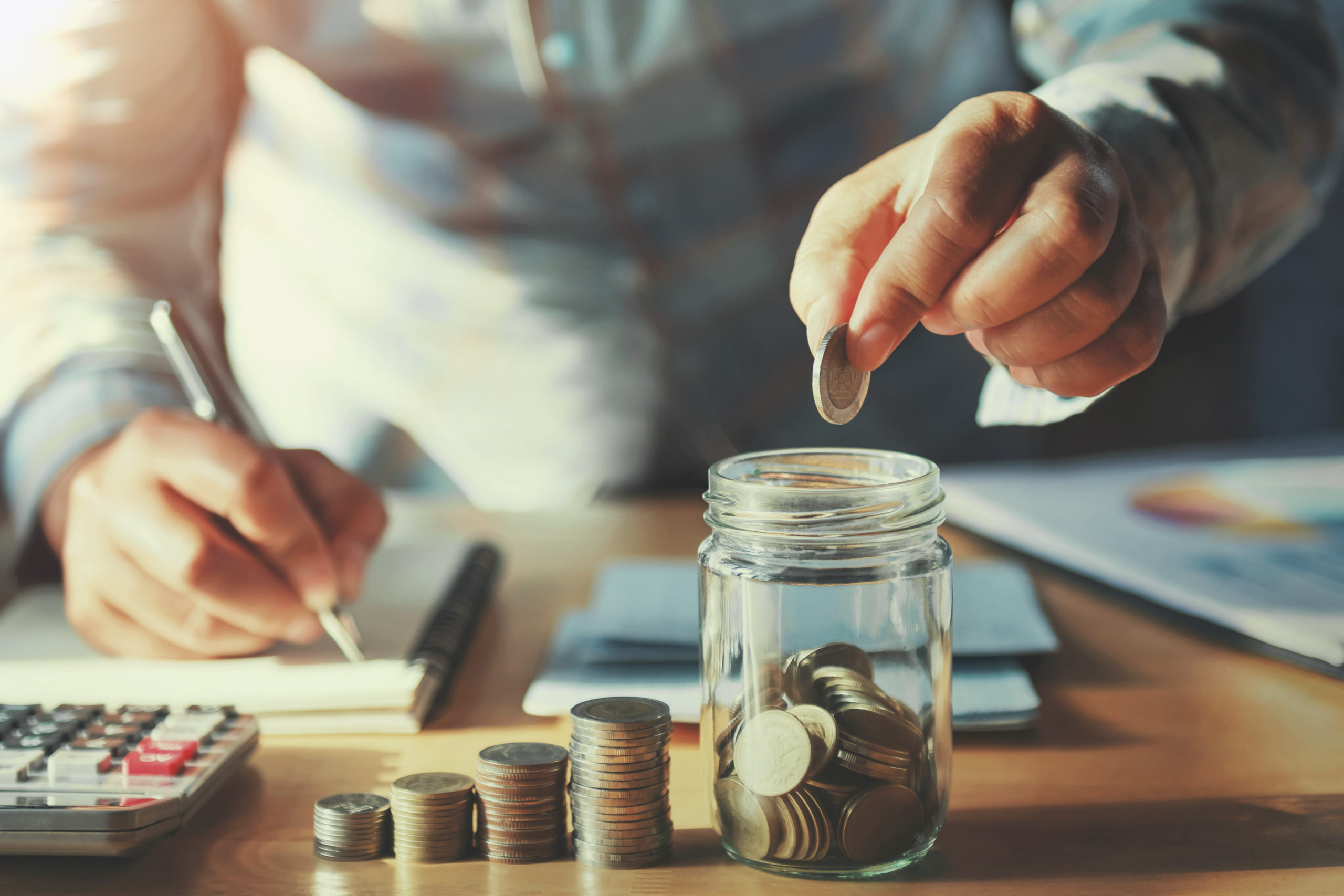 businessman saving money concept. hand holding coins putting in jug glass