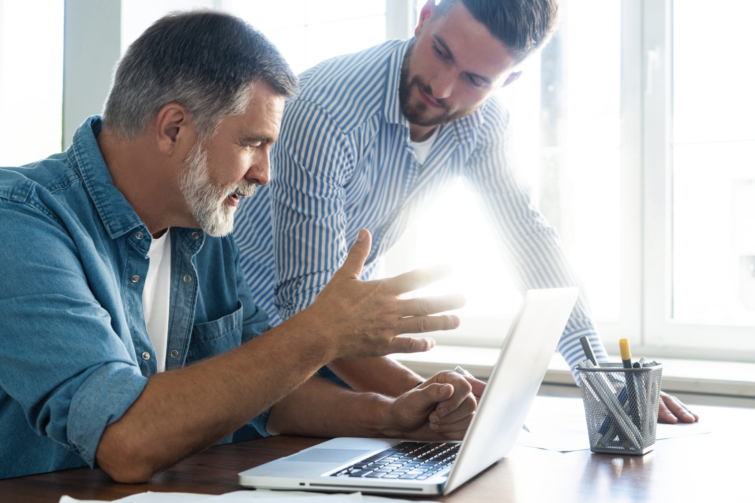 Sharing experience with colleague. Two business men discussing something and looking at laptop. Handsome two colleagues are working in cooperation