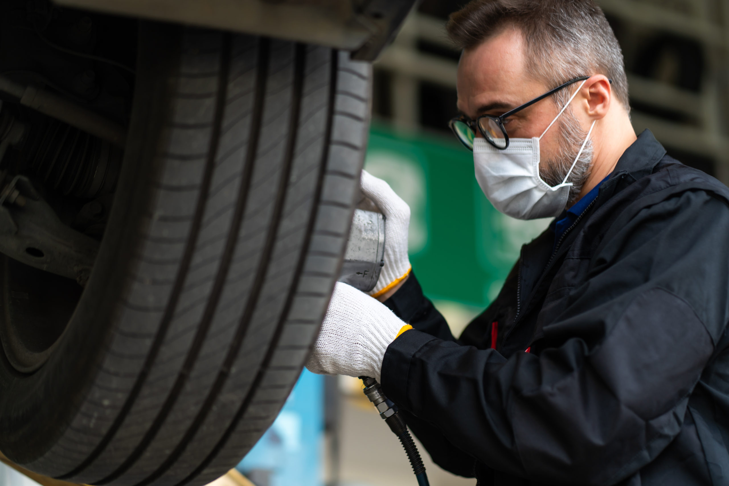 Professional car mechanic changing car wheel at Car maintenance and auto service garage. Caucasian man worker people. Surgical face mask protec coronavirus covid 19.