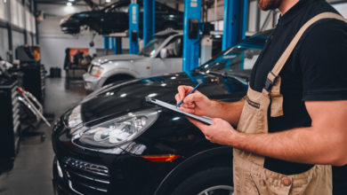 Cropped image of handsome mechanic in uniform making notes while standing in auto service. Side view.