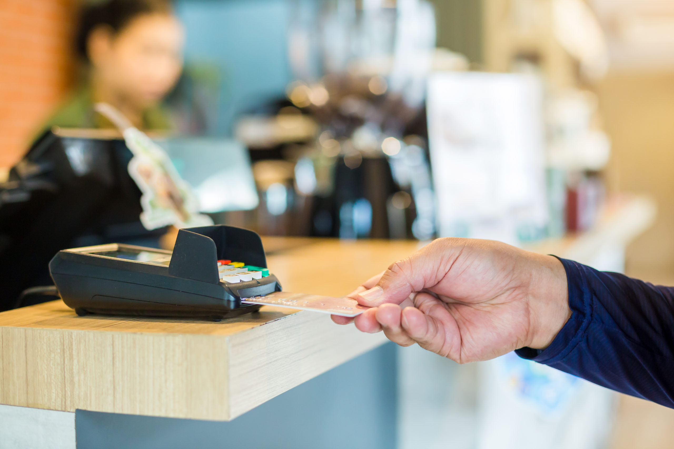 Hand put credit card In slot of credit card reader with blurry cashier at counter service, credit card payment, buy and sell products & service, the concept of payment without cash, selective focus.