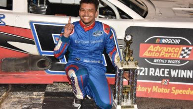 driver kneeling in front of race car with trophy