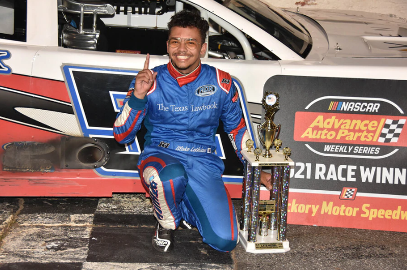 driver kneeling in front of race car with trophy