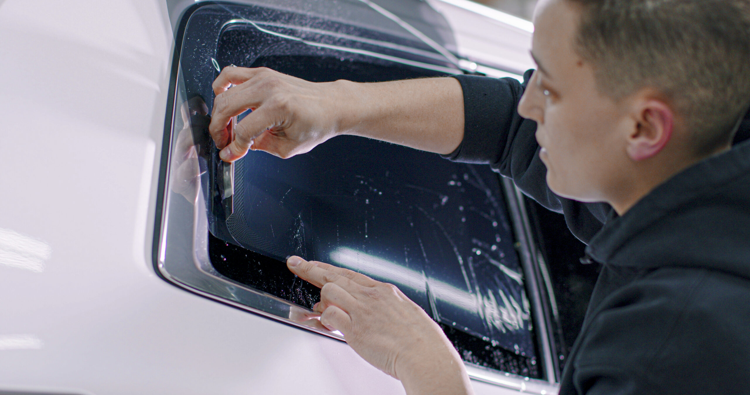 man applying window tint to car window