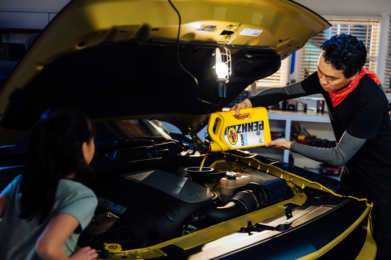 A father and daughter top off their car with Pennzoil motor oil.