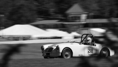 A black and white photo of an old sportscar racing on track at Lime Rock Park.