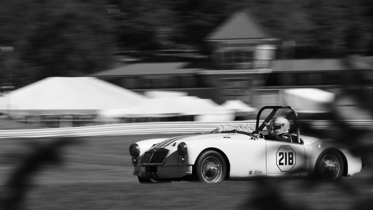 A black and white photo of an old sportscar racing on track at Lime Rock Park.