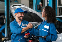 Two happy auto mechanics in uniforms working in auto service with car.