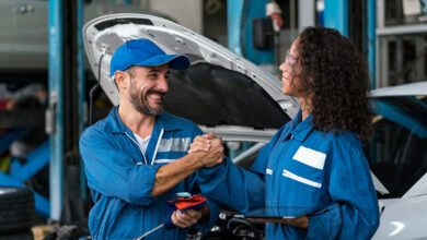 Two happy auto mechanics in uniforms working in auto service with car.