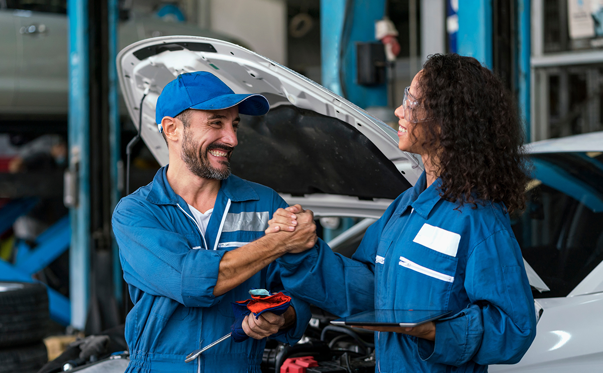 Two happy auto mechanics in uniforms working in auto service with car.