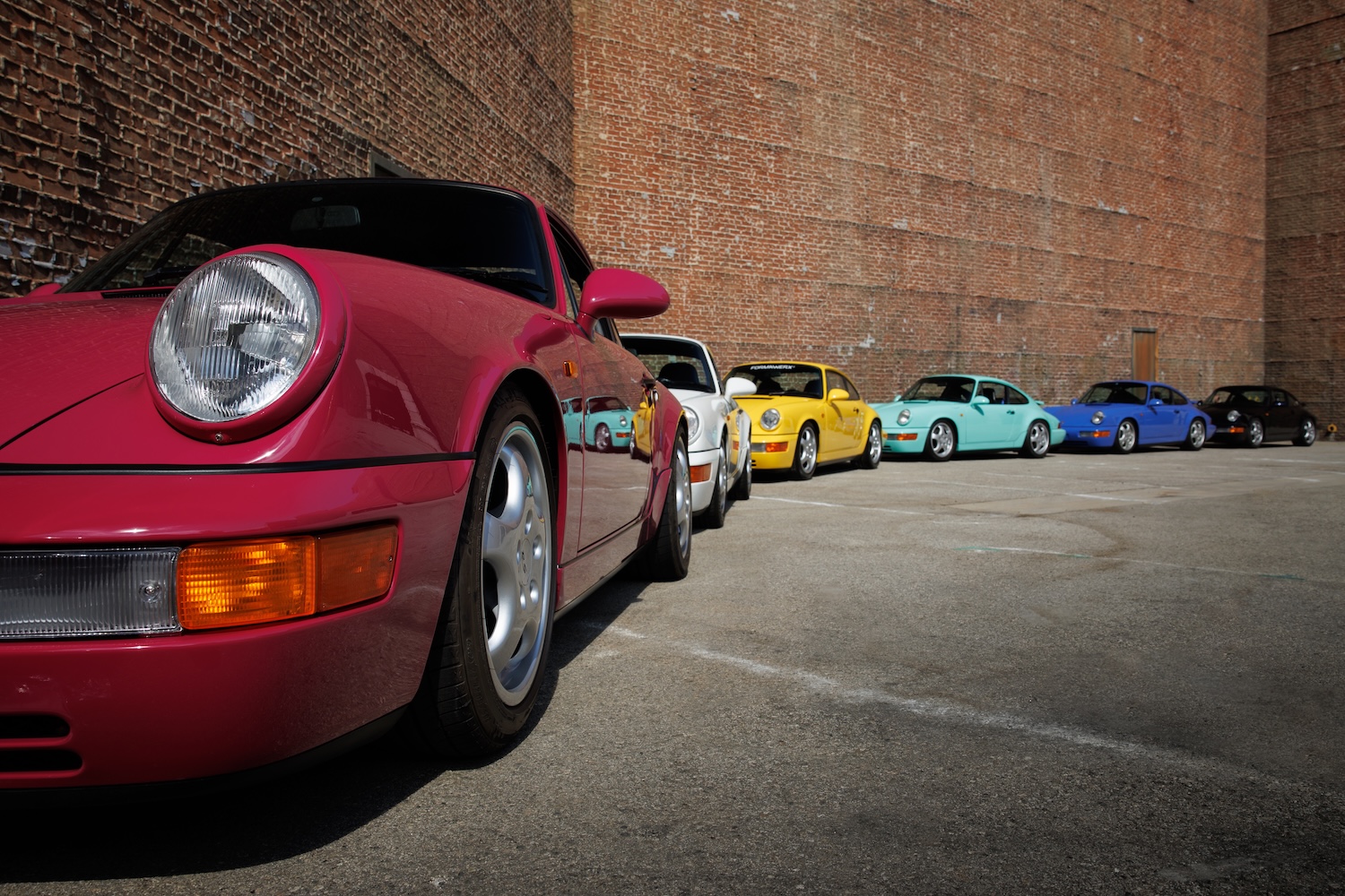 porsches of many colors lined up along a brick wall