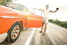 Person with tattoo taking selfie with vintage car during road trip
