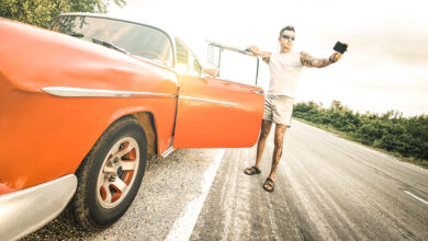 Person with tattoo taking selfie with vintage car during road trip