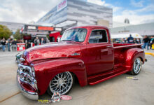 A polished red classic truck displayed at SEMA show with people