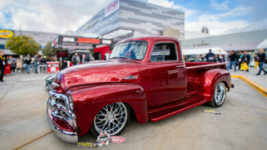 A polished red classic truck displayed at SEMA show with people