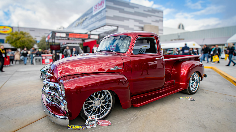 A polished red classic truck displayed at SEMA show with people