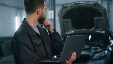 Auto mechanic holding computer and looking concerningly at car engine