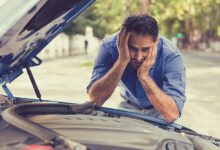 young stressed man having trouble with his broken car looking in frustration at failed engine