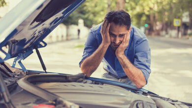 young stressed man having trouble with his broken car looking in frustration at failed engine