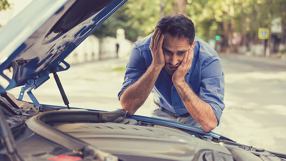 young stressed man having trouble with his broken car looking in frustration at failed engine