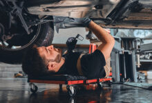 Male car mechanic worker working using wrench tool for repair, maintenance underneath car. Mechanic vehicle service checking under car in garage. Auto car repair service, maintenance concept.