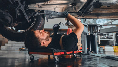 Male car mechanic worker working using wrench tool for repair, maintenance underneath car. Mechanic vehicle service checking under car in garage. Auto car repair service, maintenance concept.