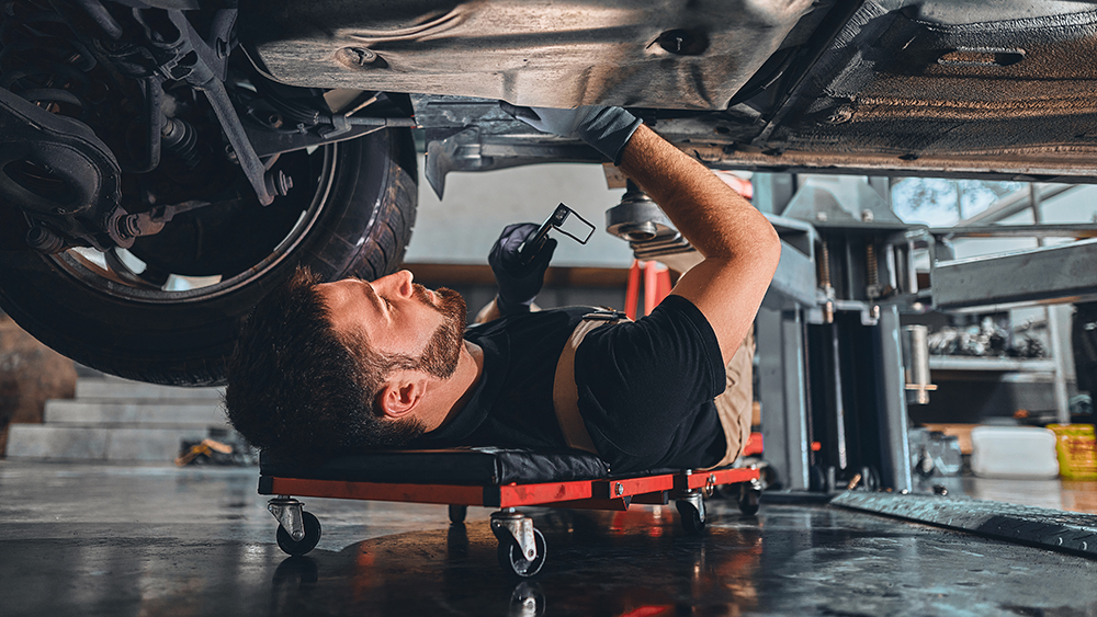 Male car mechanic worker working using wrench tool for repair, maintenance underneath car. Mechanic vehicle service checking under car in garage. Auto car repair service, maintenance concept.