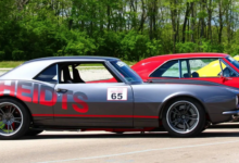 Lined of classic cars parked outside with Heidts logo on the side of first car