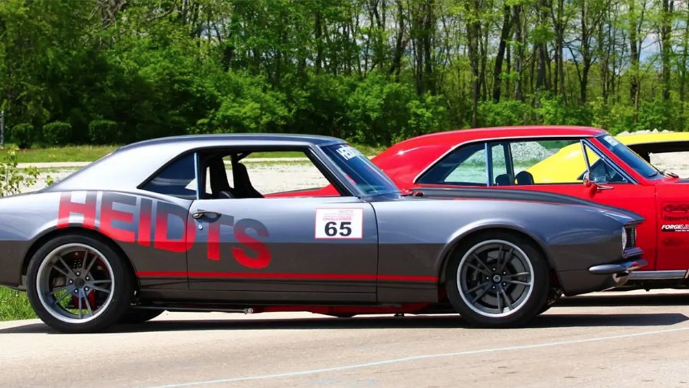 Lined of classic cars parked outside with Heidts logo on the side of first car