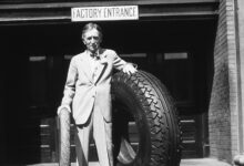 Harvey Firestone Sr. standing at the Akron, Ohio, factory entrance with an original Firestone non-skid tread tire and a large tire, ca. 1926-30.