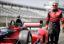 Mario Andretti walking next to race car on racetrack