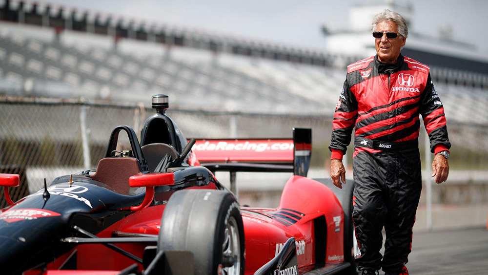 Mario Andretti walking next to race car on racetrack