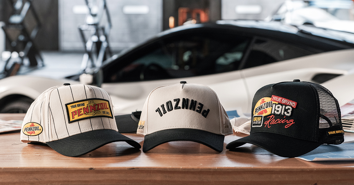 True Brvnd Pennzoil baseball caps sitting on table with car in background