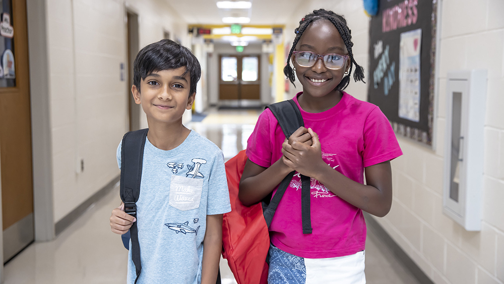 Two young students with backpacks in school hallway
