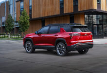 Red 2025 Chevrolet Equinox RS driving in front of building