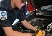 Student auto mechanic working under the hood of a car crop