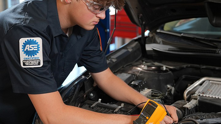 Student auto mechanic working under the hood of a car crop