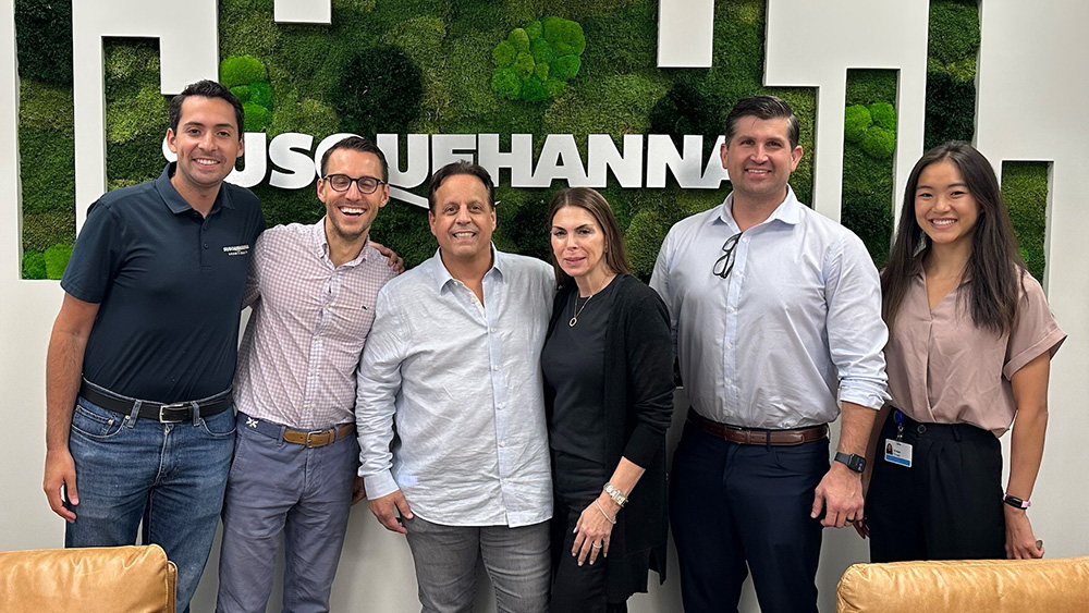 Susquehanna Growth Equity and Tint World reps in front of Susquehanna logo on wall