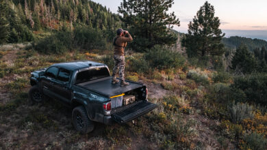 Man standing on truck bed cover looking through binoculars on a mountain