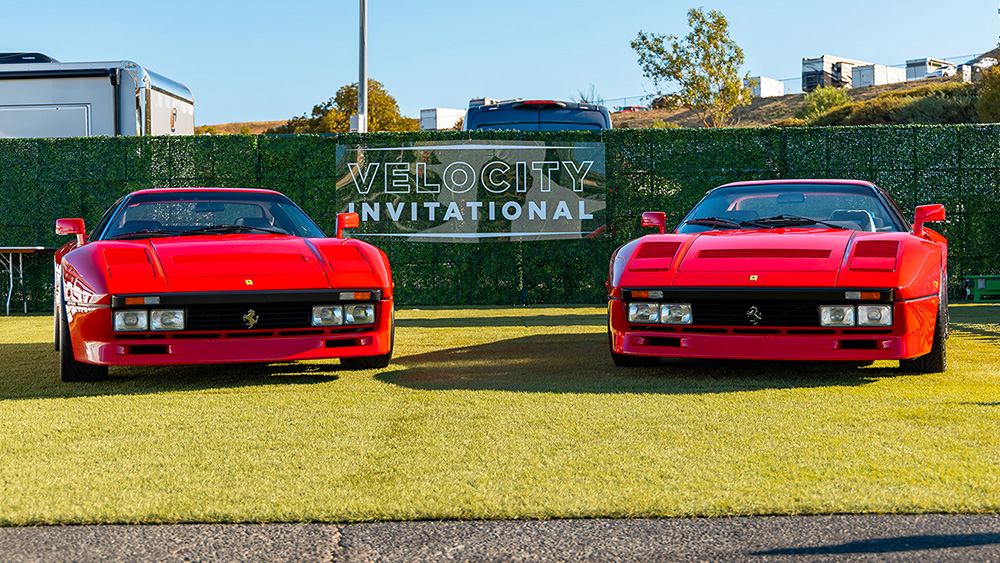 Two red Ferraris parked in front of Velocity International sign