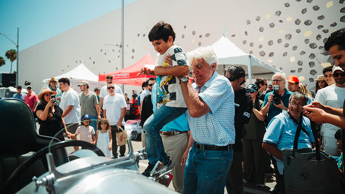 Jay Leno helping young child into classic car
